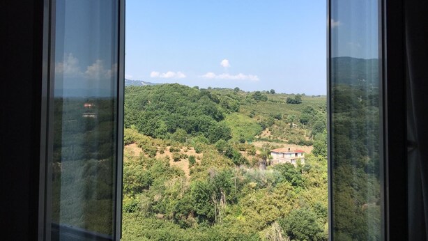 A view from a window overlooking a lush green landscape with a few scattered buildings. - LARGE APARTMENT 60 KM FROM ROME (Vignanello)