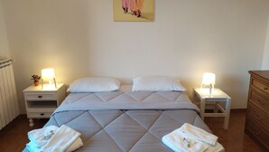 A neatly made bed with a quilted headboard, two bedside tables with lamps, a wooden dresser, and a wall-mounted painting. - LARGE APARTMENT 60 KM FROM ROME (Vignanello)