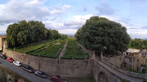 A historic site with a well-maintained garden, stone walls, and a paved road with parked cars.