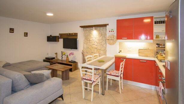 A compact living space with a sofa, dining table, chairs, a kitchen area with red cabinets, and a refrigerator. - Apartment Maja 2 (Premantura)