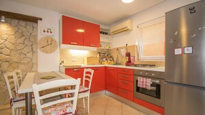 A kitchen with red cabinets, a stainless steel refrigerator, and a dining table with chairs. - Apartment Maja 2 (Premantura)