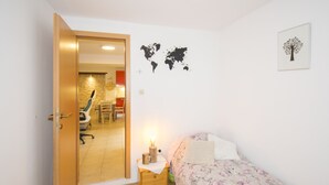 A bedroom with a wooden door, a bed with a floral bedspread, a nightstand with a lamp, and a world map on the wall. - Apartment Maja 2 (Premantura)