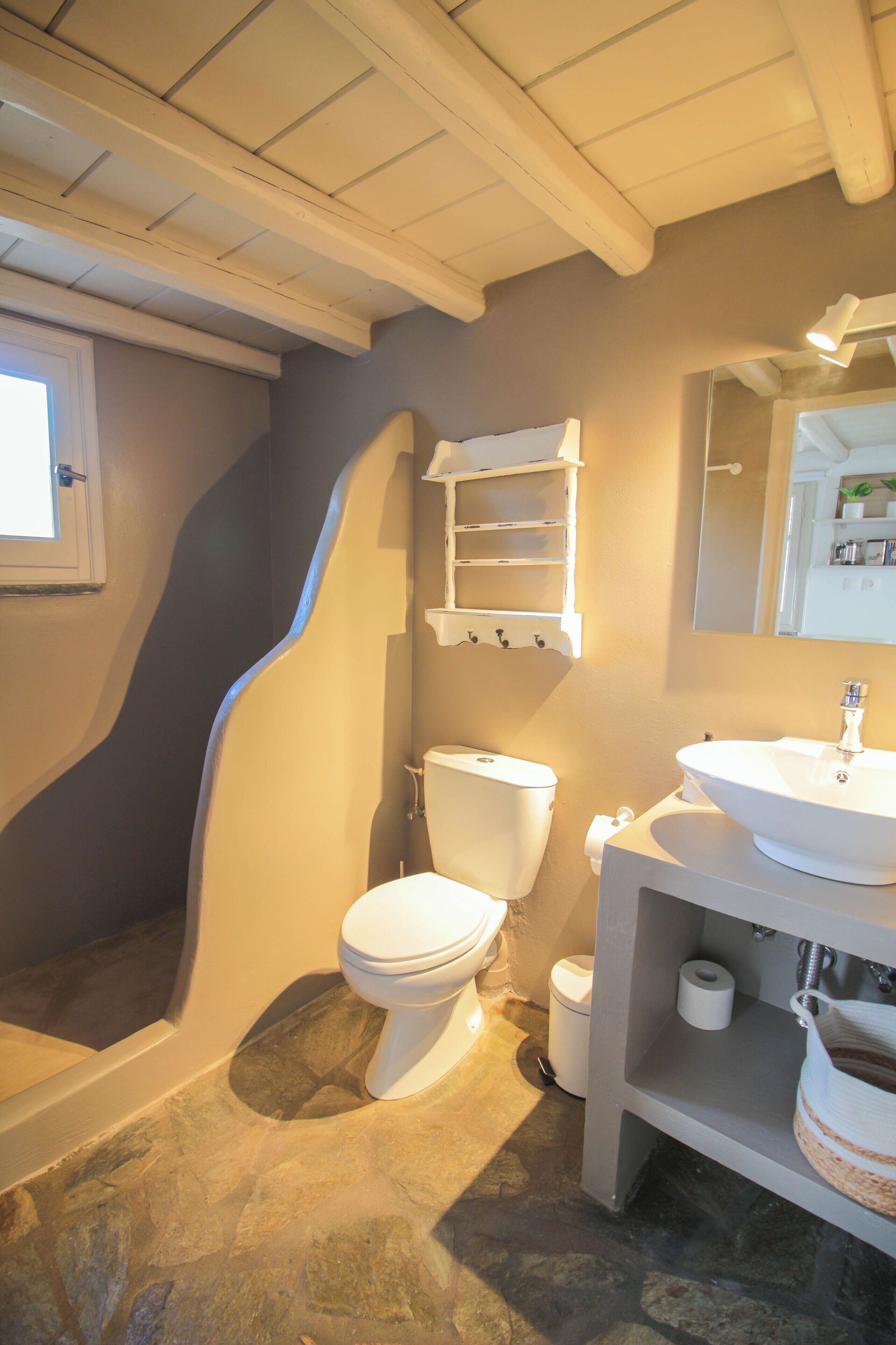 A bathroom with a stone floor, white fixtures, a built-in shelf, and a window.