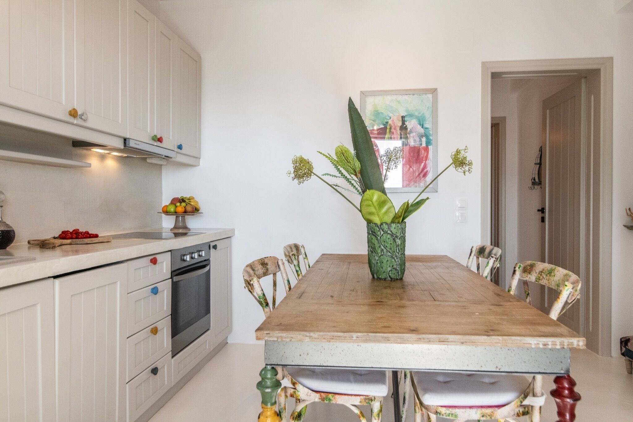 A kitchen with white cabinets, a wooden dining table, and a vase with flowers.