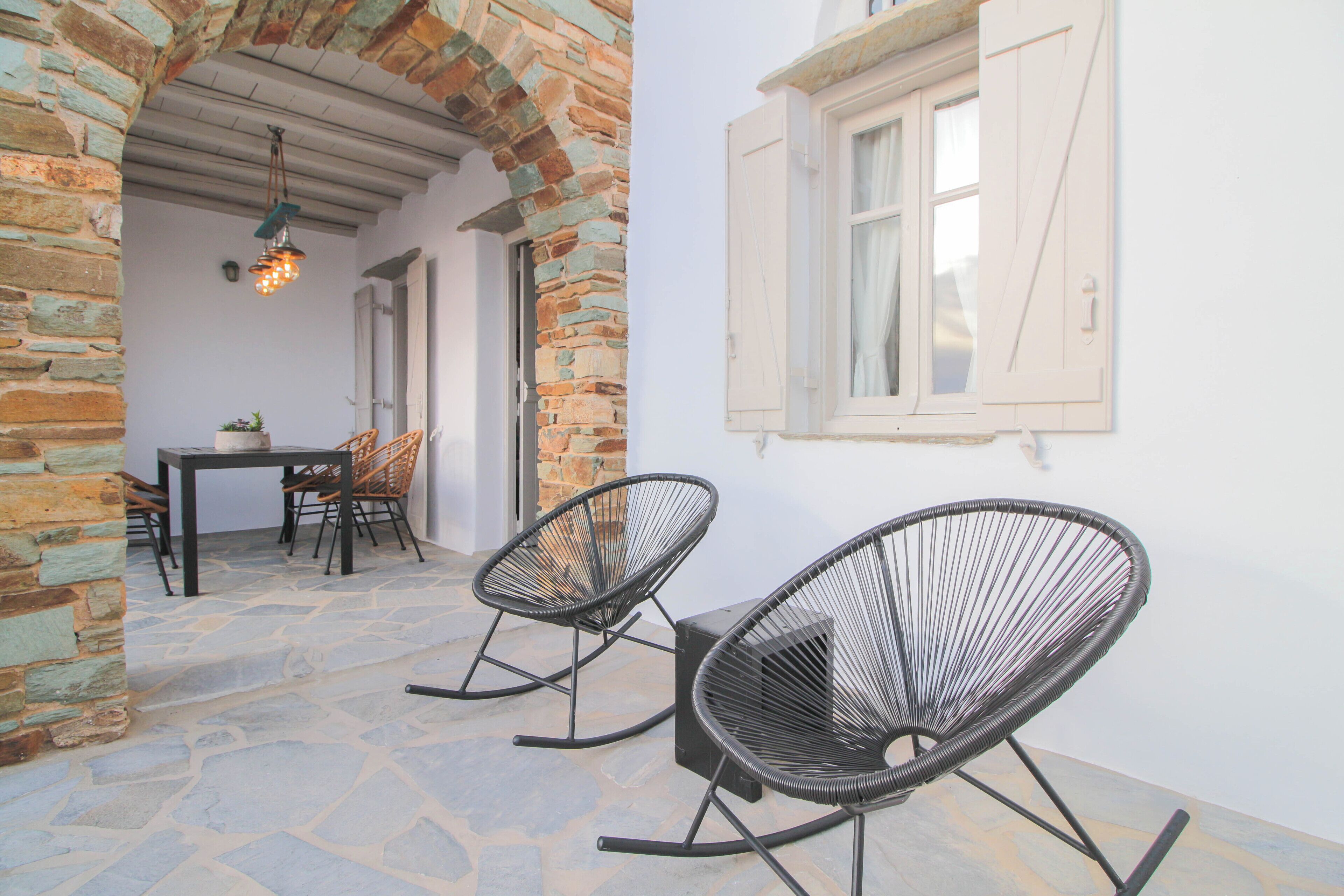 A stone-floored patio with two black rocking chairs, a table, and chairs.