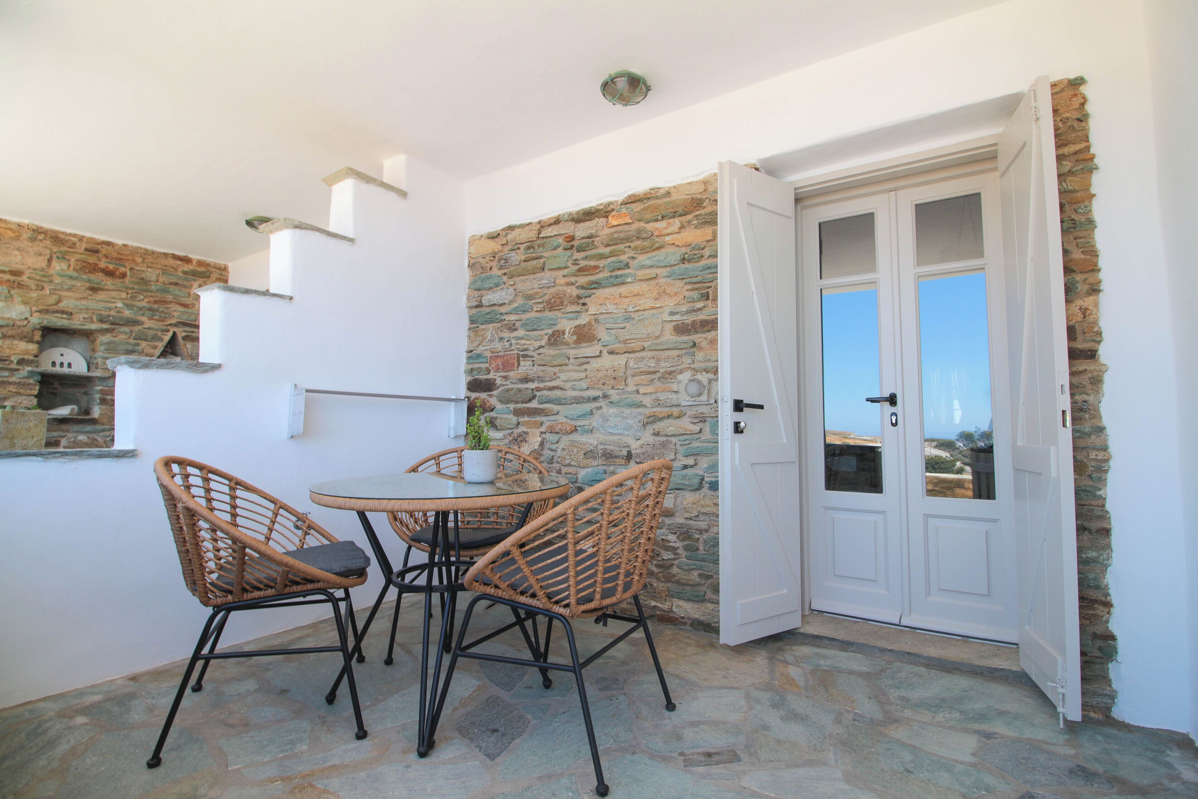 A dining area with wicker chairs and a table, a stone wall, and a white door with glass panels.