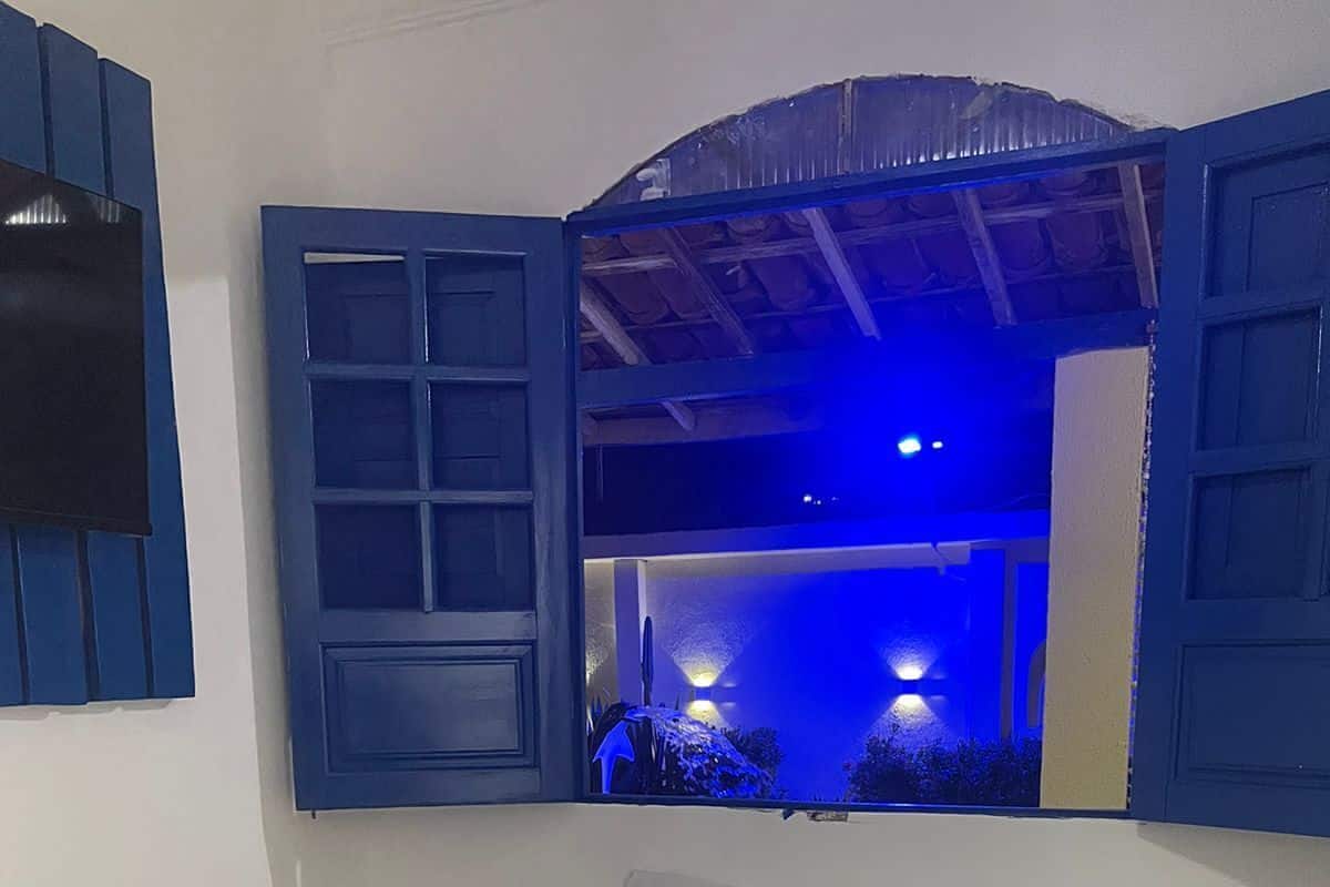 Un dormitorio con cama, mesita de noche, espejo y vista a un espacio exterior con iluminación azul.