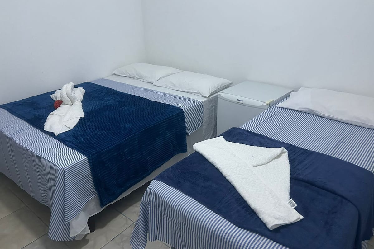 Habitación de hotel con dos camas individuales, cada una con colcha a rayas y almohadas blancas. En cada cama, un pequeño mesita de noche con una lámpara blanca.