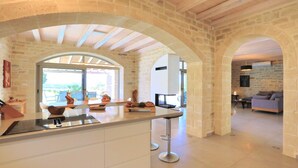 A modern kitchen with stone arches, a central island, and a dining area with a sofa and table. - Luxury villa with a fantastic view, the pool can be heated (Rethymnon)