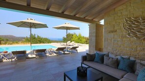 Una zona de piscina amb gandules, ombrel·les i un sofà.