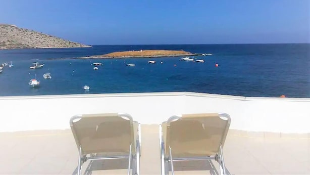 A terrace with two metal chairs facing a sea view with boats and a rocky island. - Remarkable 3double-bed House in Daskalio (Lavreotiki)