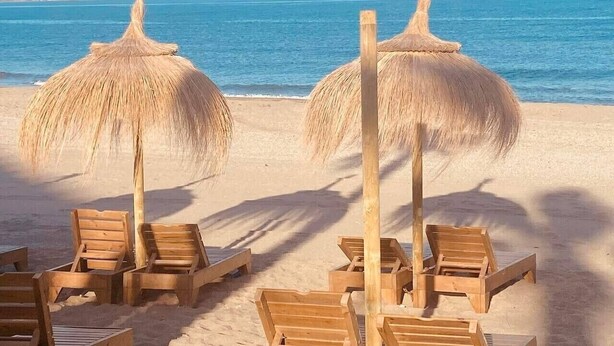 A beach with wooden lounge chairs and thatched umbrellas.