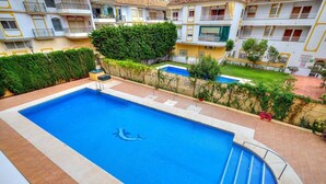 A swimming pool with a dolphin design, surrounded by a tiled deck and a hedge.