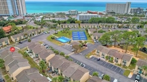 Vue aérienne d’un quartier résidentiel avec une piscine, des parkings et des immeubles offrant une vue sur l’océan.