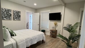 Un dormitorio con una cama, un televisor montado en la pared y una planta en maceta.