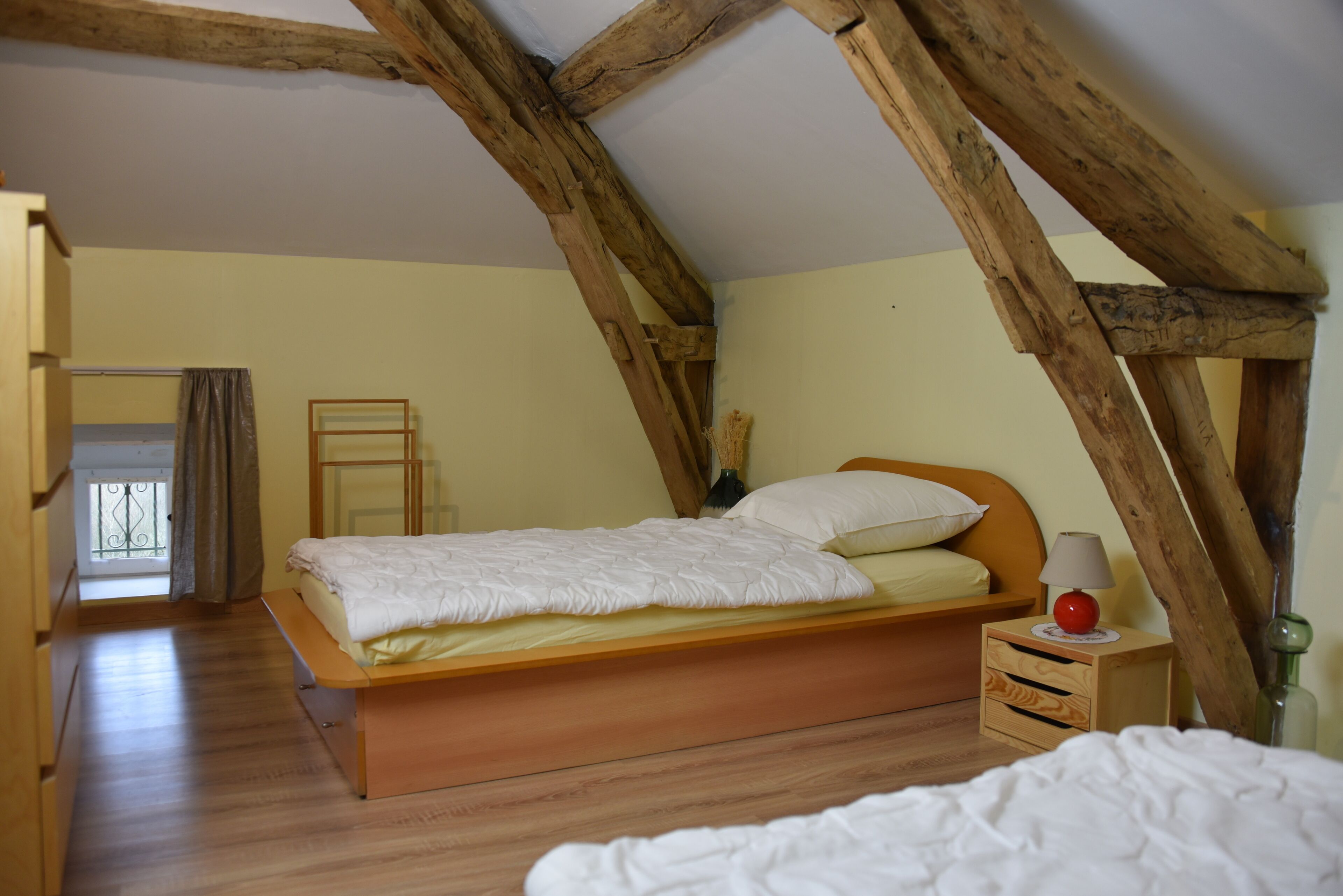 Un dormitorio con una cama de madera, una mesita de noche con lámpara y una ventana con cortinas.