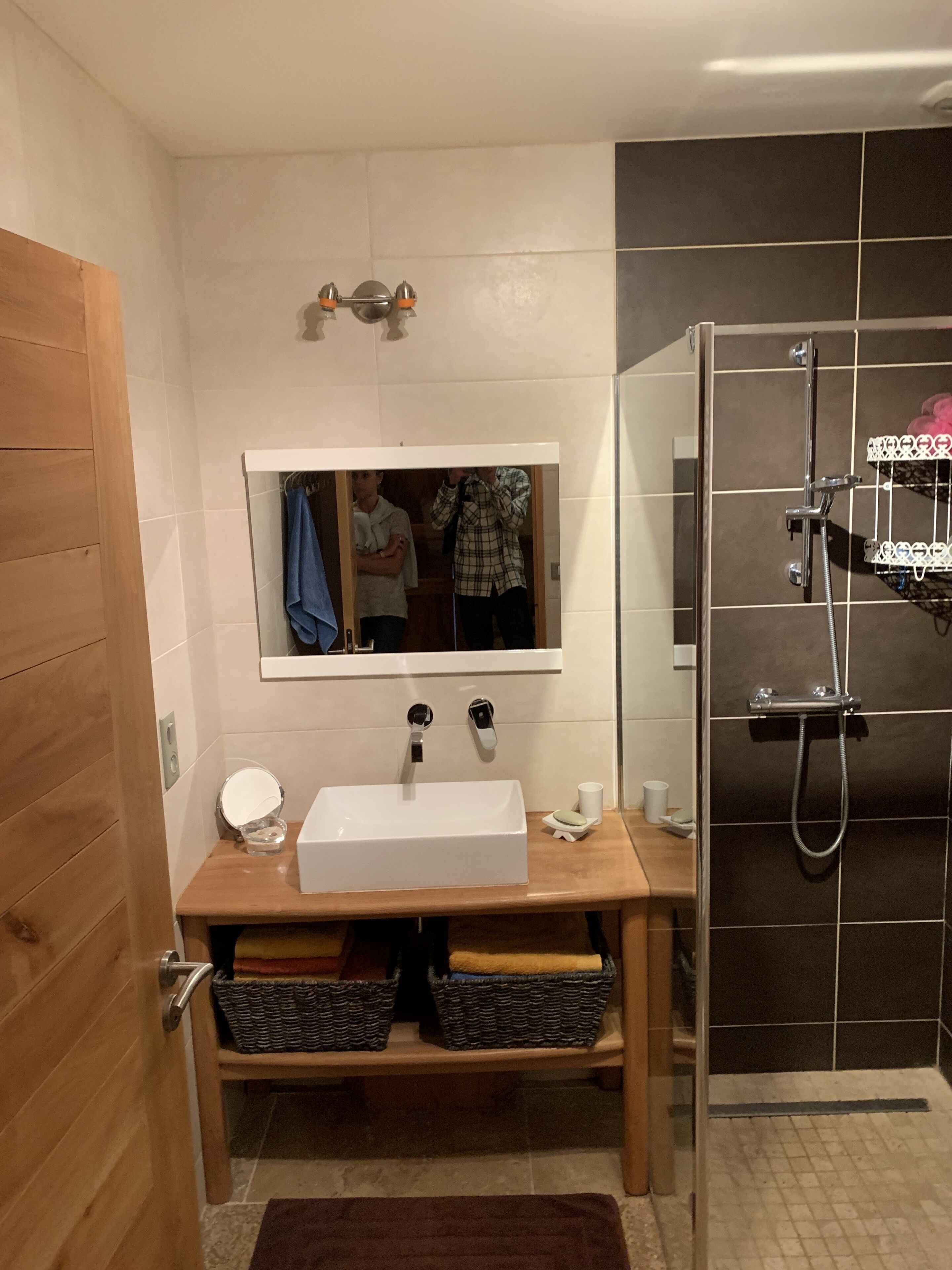 A bathroom with a white sink, mirror, and shower. There are baskets under the sink and a towel rack above it.