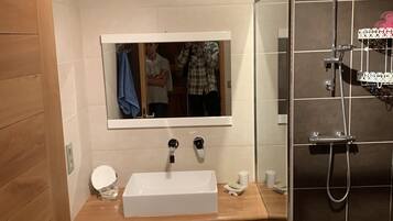 A bathroom with a white sink, mirror, and shower. There are baskets under the sink and a towel rack above it.