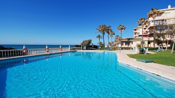 Ein großer, klarer blauer Pool mit weißer Liegefläche und Rettungsbojen, umgeben von Palmen und Blick auf den Ozean.