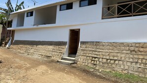 A two-story building with a white exterior, a stone foundation, and a metal roof.