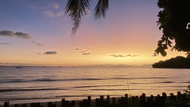 A beach scene with a wooden fence, calm sea, and a sunset.