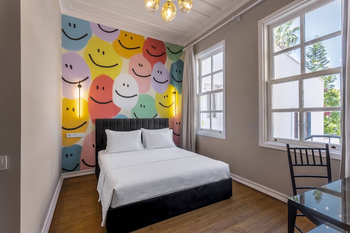 Quarto com cama, janela e parede decorada com carinhas sorridentes.