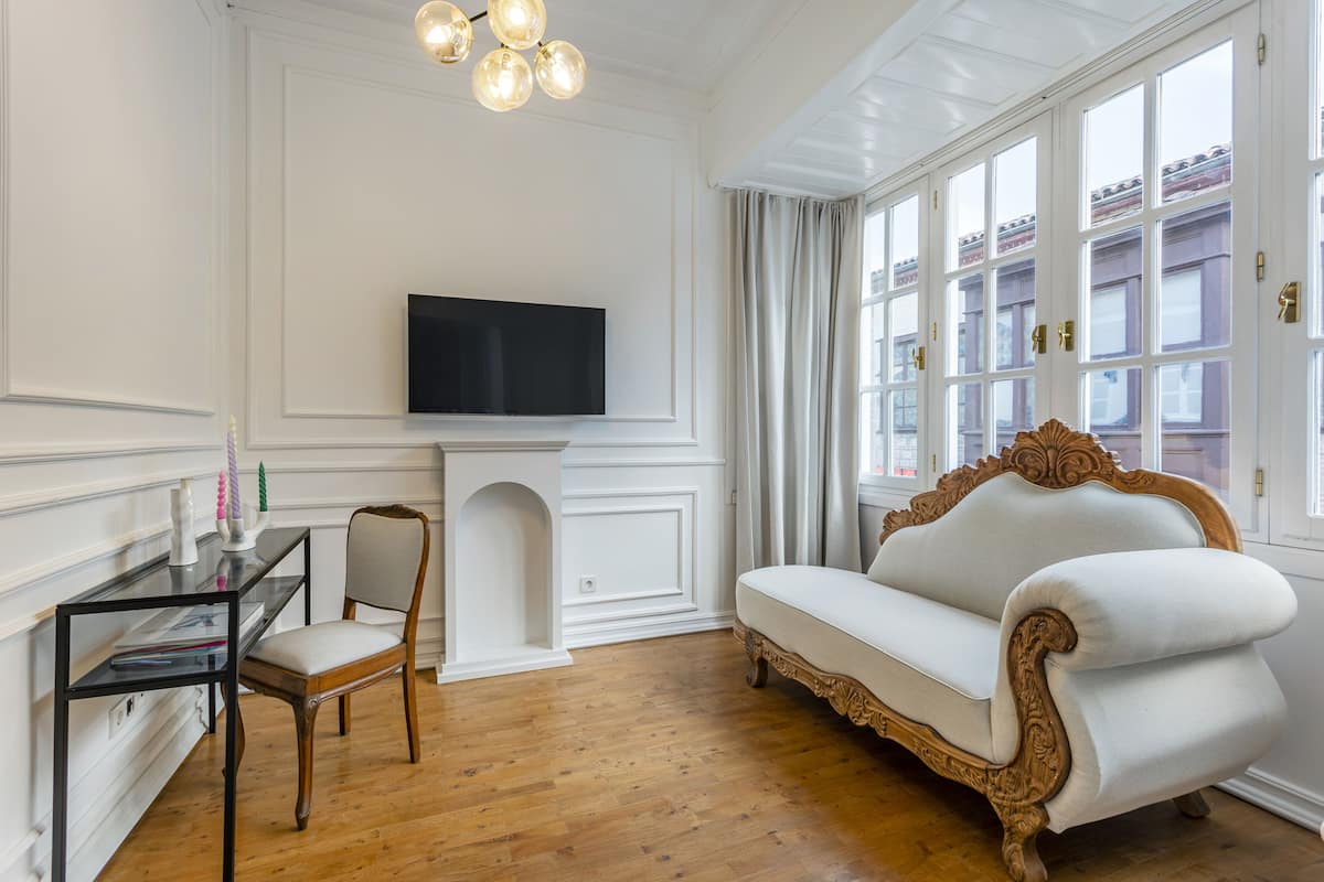 Quarto com sofá branco, televisão na parede, cadeira de madeira e mesa de vidro.