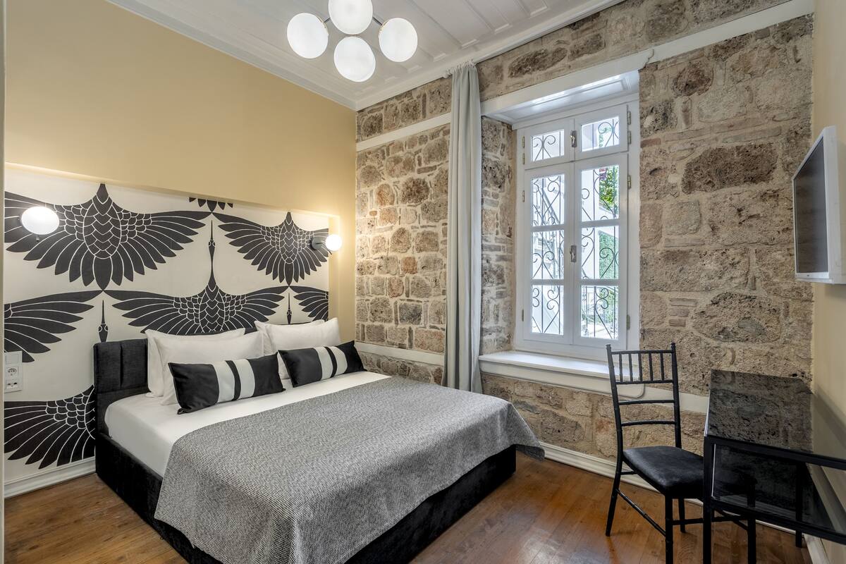 Quarto com cama, uma cadeira, parede de pedra e janela.