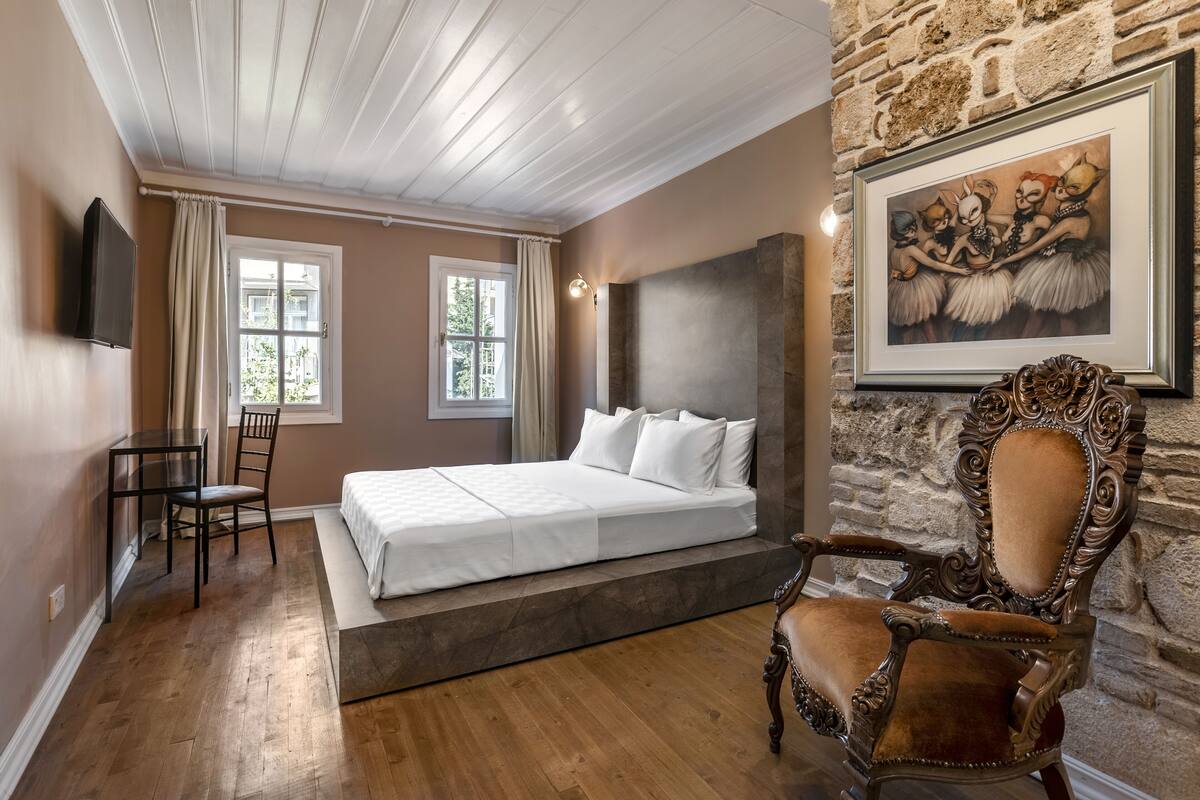 Quarto com cama, cadeira, escrivaninha e parede de pedra.