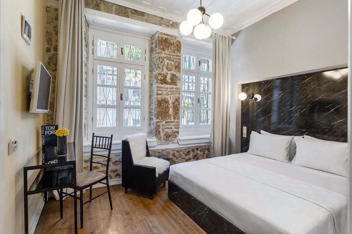 Quarto com cama grande, uma cadeira, escrivaninha e parede de pedra.