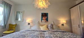 Een slaapkamer met een bed, een stoel, een schilderij en twee wandlampen.