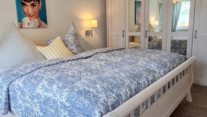 A bedroom with a large bed, a wardrobe, a mirror, and a wall-mounted light fixture.