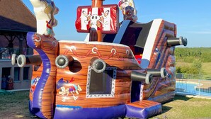 A large inflatable pirate ship with a steering wheel and a skull and crossbones flag. - Les SOURCES Premium, SPA, Swimming pool, Fishing pond, Playground, Games room... (Hautefort)