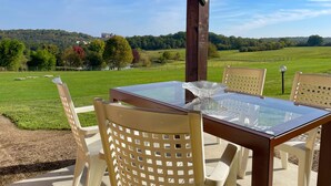 A glass-top table with four chairs, set outdoors with a view of a green field and trees. - Les SOURCES Premium, SPA, Swimming pool, Fishing pond, Playground, Games room... (Hautefort)