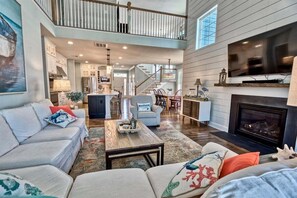 A spacious living room with a high ceiling, a fireplace, a television, and a staircase leading to an upper level.
