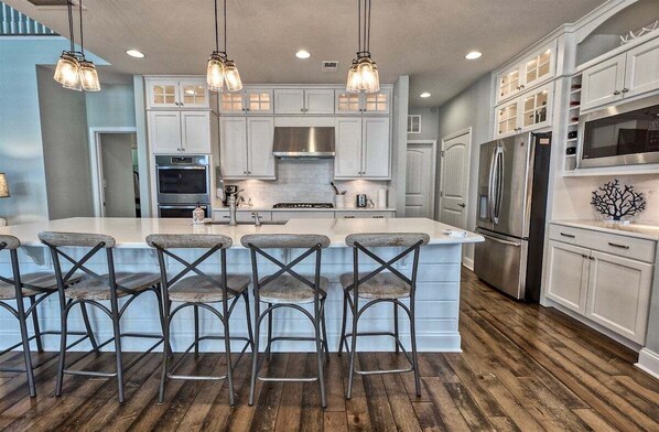 A kitchen with a central island, bar stools, stainless steel appliances, and pendant lighting.