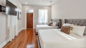 A bedroom with two beds, a ceiling fan, a TV mounted on the wall, and a wooden door. - Historical Charm with Modern Touch 5 Bedrooms 4 Bathrooms, Centrally Located (New Orleans)
