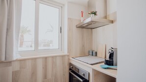 Een compacte keuken met een raam, houten lambrisering, een inbouwoven en een koffieapparaat.