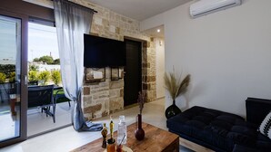 A living room with a stone wall, a flat-screen TV, a dark sofa, and a wooden coffee table. - Stone project villa, pool,near tavern,supermarket (Pigi)
