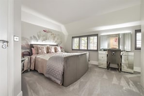 A bedroom with a bed, dresser, vanity, and a large mirror.