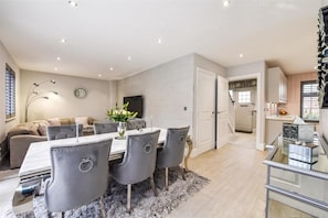 Una sala de estar moderna con comedor, un conjunto de sofás y una cocina visible a través de una puerta abierta.