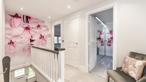 A hallway with a staircase, a white door, and a wall with a floral mural. - Barfoot Close (Waterlooville)