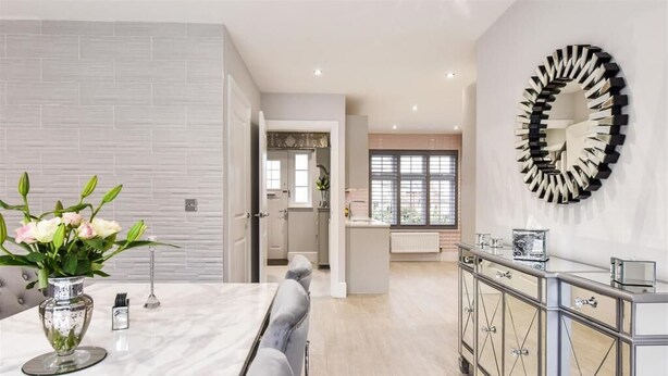A modern kitchen with a marble countertop, a dining area with a gray sofa, and a kitchen island with a mirror. - Barfoot Close (Waterlooville)