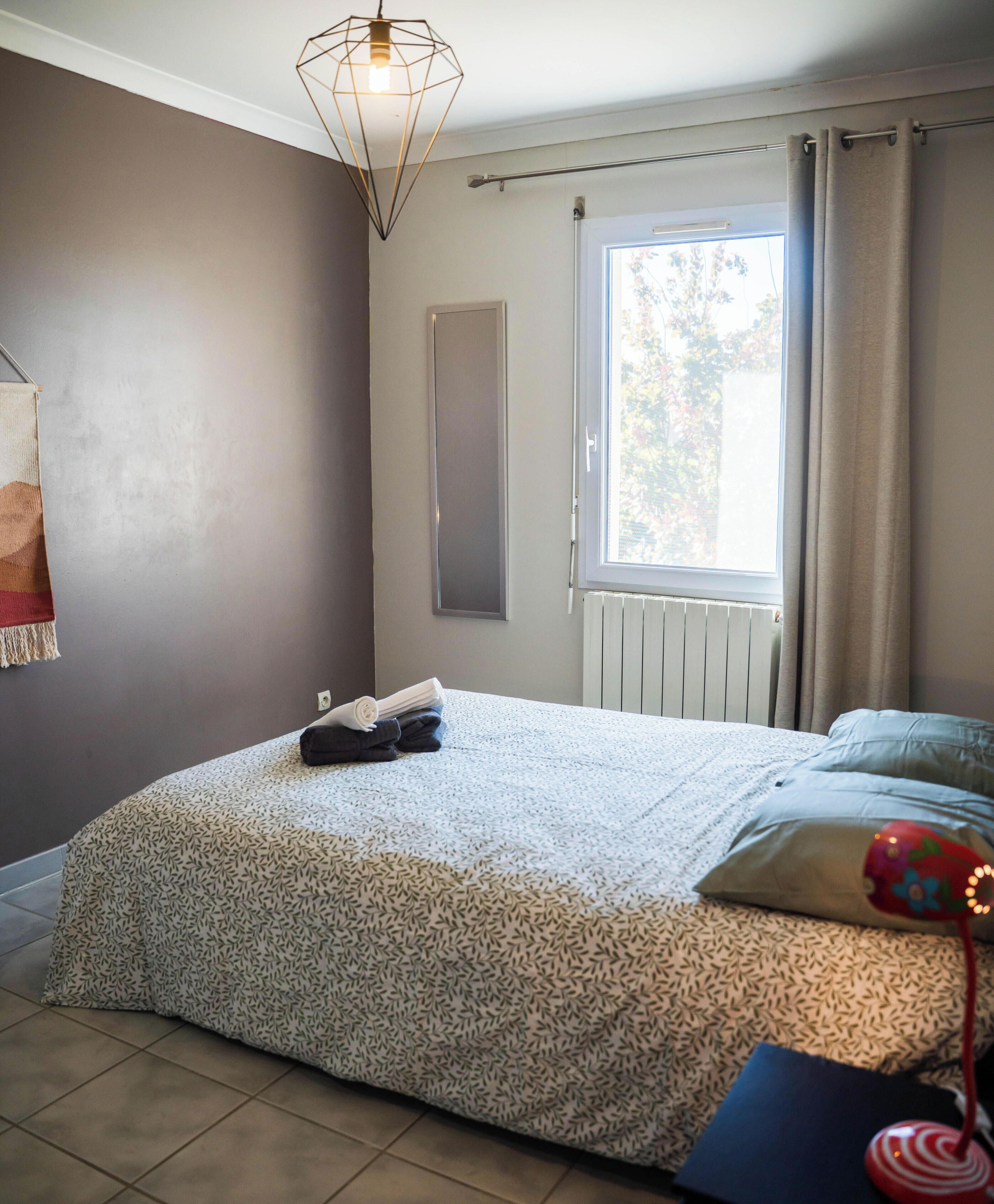 Un dormitorio con cama, ventana, radiador y lámpara colgante.