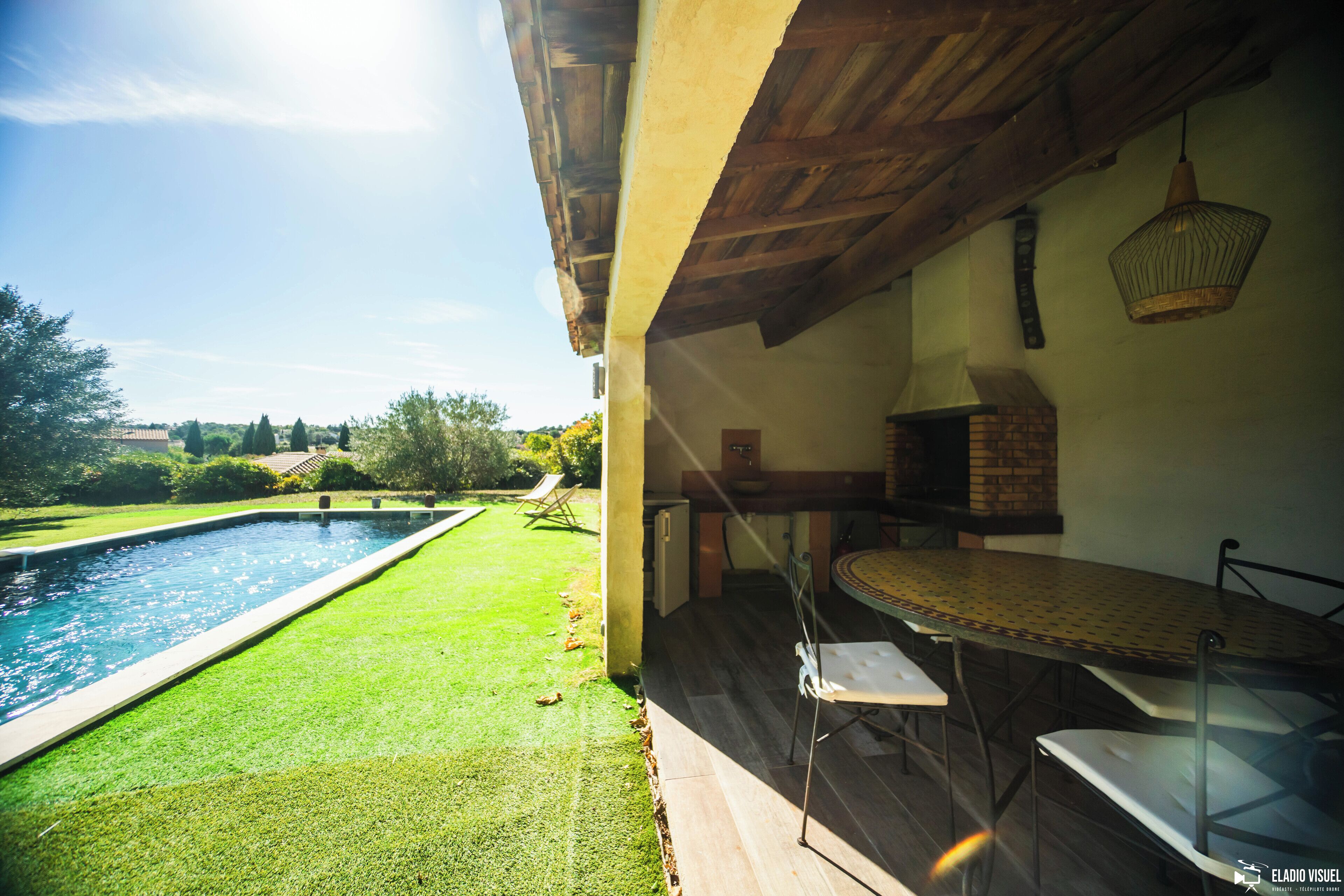 Un espace aménagé au bord de la piscine, avec une table et des chaises, un four en briques et une vue sur le paysage environnant.