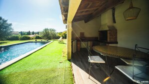 A poolside area with a table and chairs, a brick oven, and a view of the surrounding landscape. - Villa (Poulx)