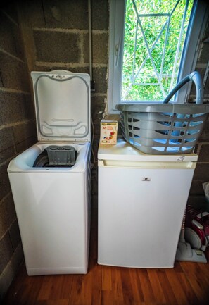 A compact laundry room with a washing machine and dryer, a window with a view of greenery, and a basket on the dryer.