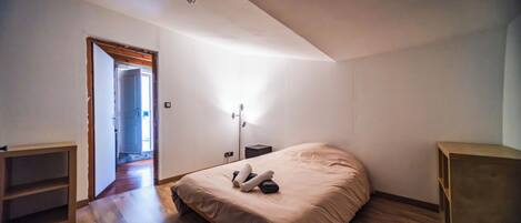 Un dormitorio con cama, mesita de noche, lámpara y suelo de madera.