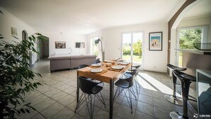 A dining area with a table set for six, surrounded by chairs, in a bright room with a view of the outdoors. - Villa (Poulx)