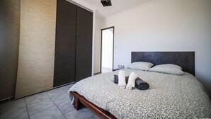 A modern bedroom with a large bed, a dark headboard, and a hanging light fixture. - Villa (Poulx)